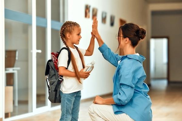 Young student and her teacher high fiving outside a classroom